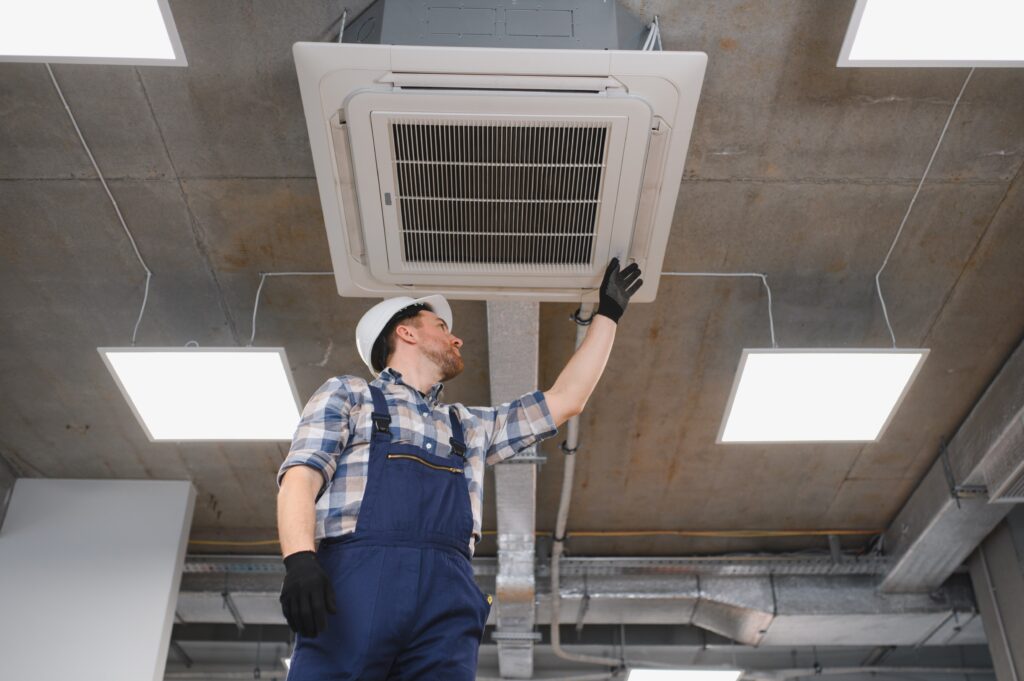 HVAC technician inspecting ceiling-mounted air conditioning unit in an office building