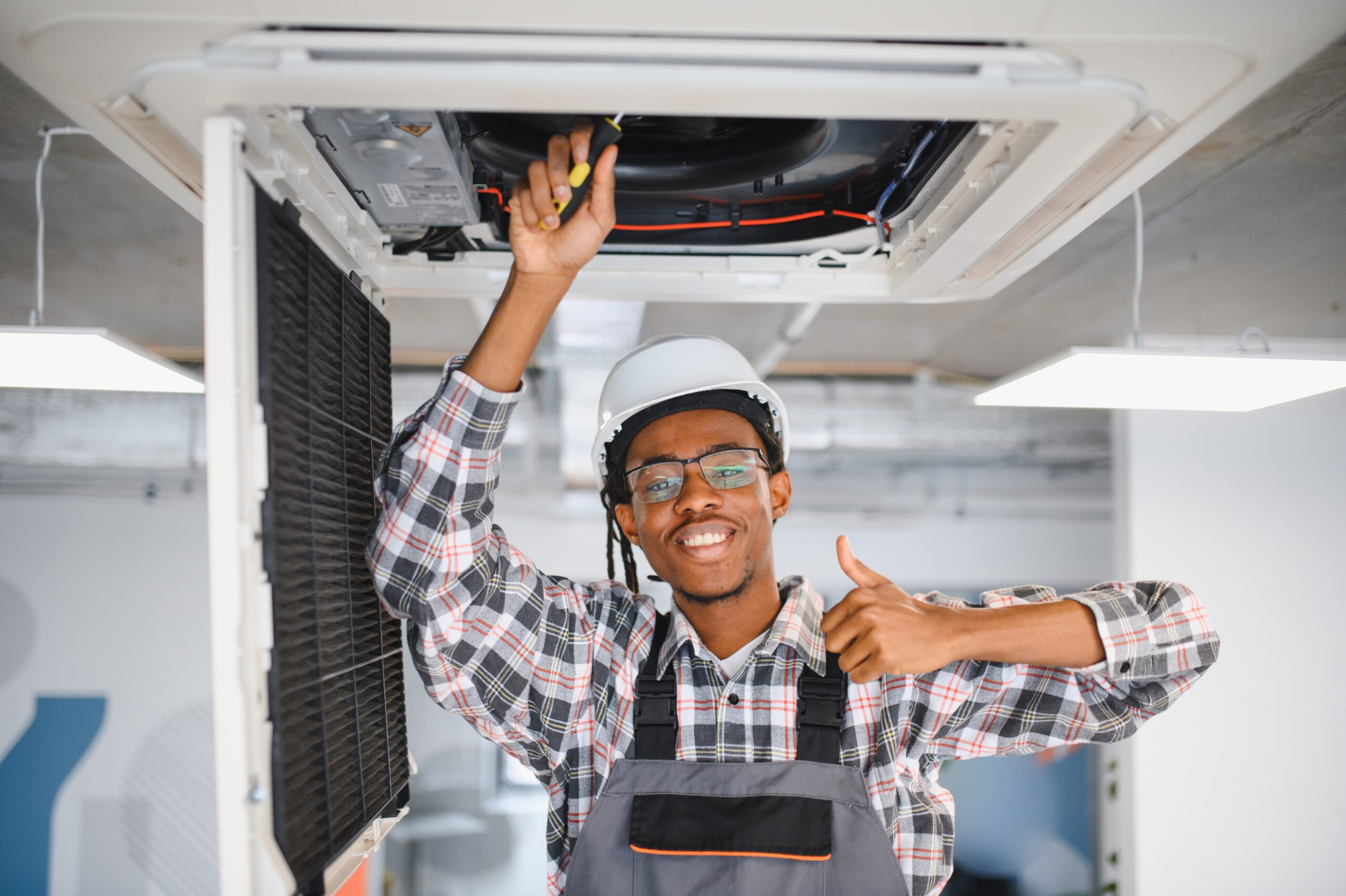 Smiling HVAC technician giving thumbs up while repairing a ceiling air conditioning unit
