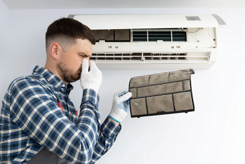 Man holding a dirty air conditioner filter and covering his nose due to bad odor from AC system