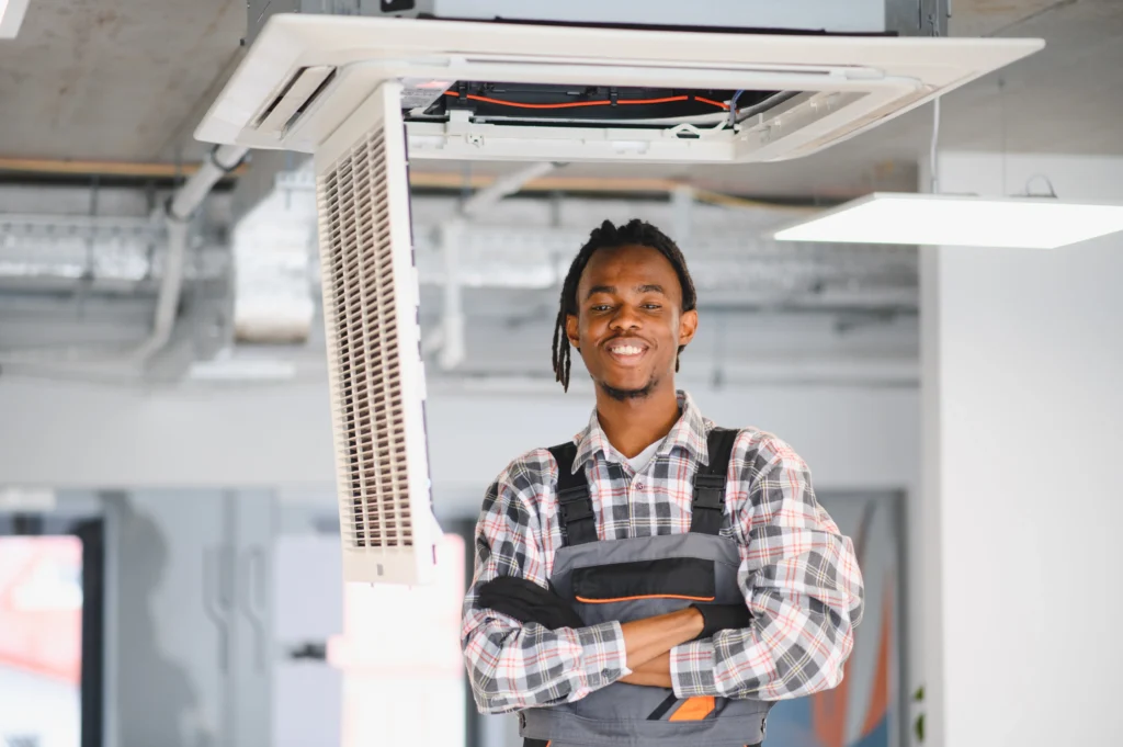 Smiling HVAC technician standing near air conditioning unit, ready for seasonal maintenance.