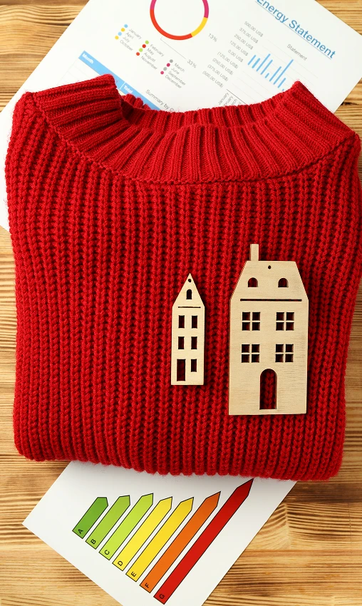 Folded red knit sweater with wooden house icons placed on home energy efficiency report, conceptual flat lay image