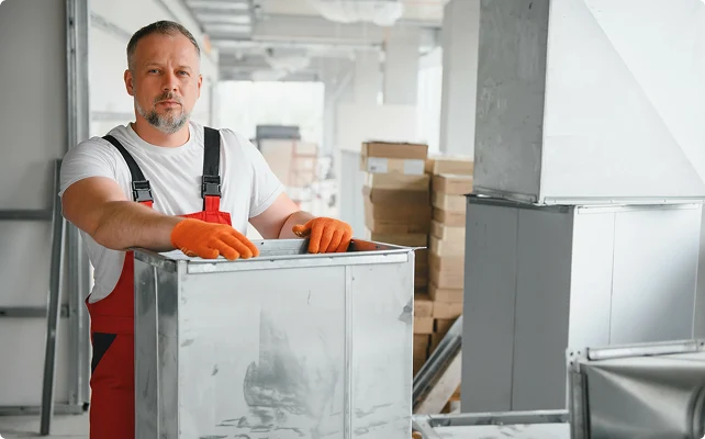 HVAC technician holding a metal air duct section during installation work