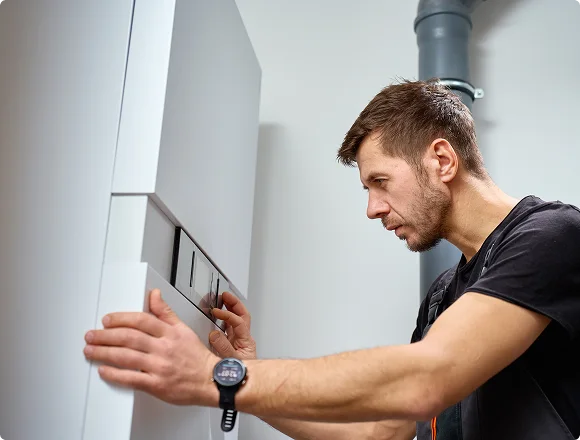 Man checking a white boiler, wearing a black t-shirt and wristwatch