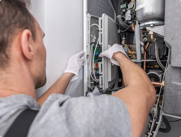 A technician wearing gloves repairs a boiler, focusing on internal wiring and components. The scene conveys precision, expertise, and technical work.