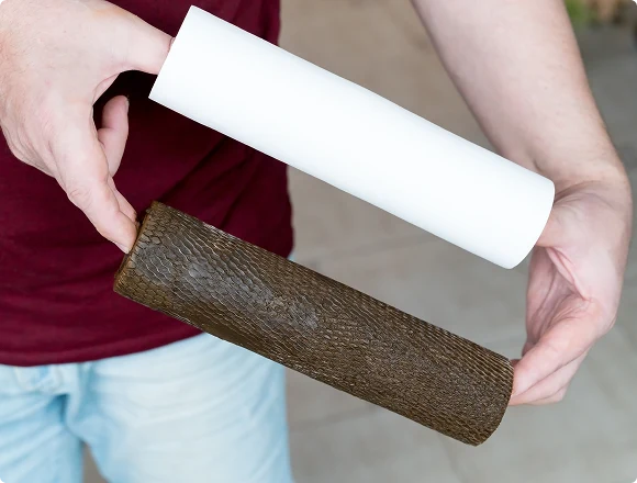 Two hands hold cylindrical objects horizontally: one white and smooth, the other textured and brown, contrasting textures and colors. Casual setting.