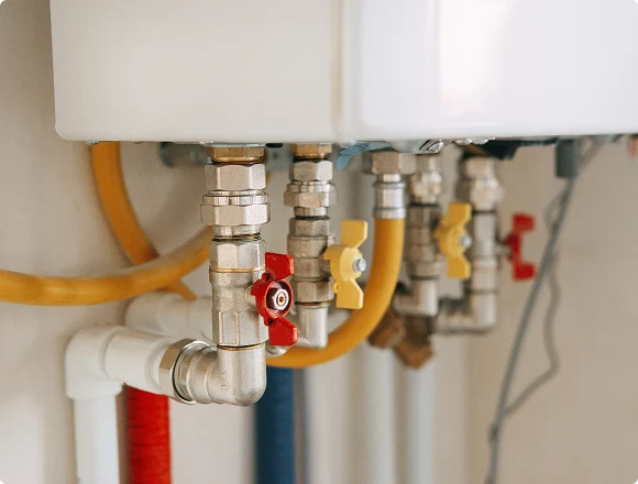 Close-up of metal pipes connected to a boiler with red and yellow valve handles, conveying a sense of technical precision and functionality.