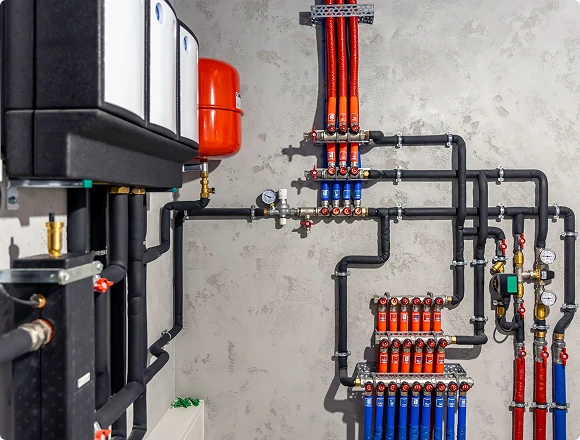 Detailed view of underfloor heating manifold with connected pipes, valves, and pressure gauges in technical room