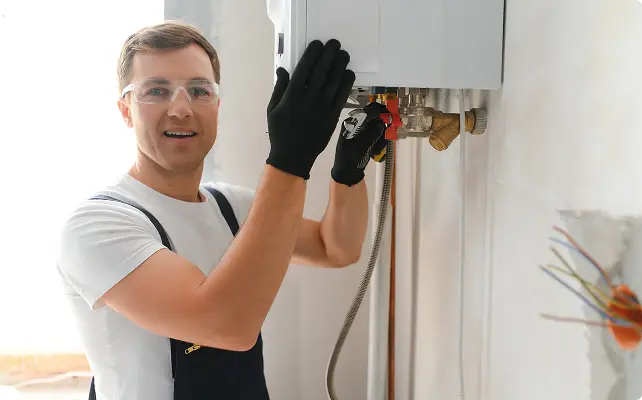 Technician installing a water heater connection while wearing safety gloves.