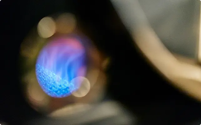 Close-up of a blue gas flame burning inside a heating unit.