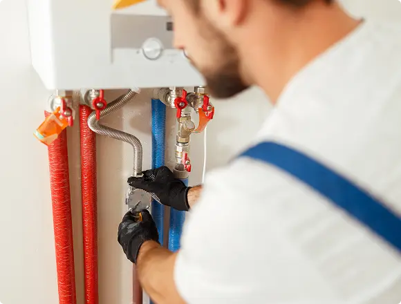 Technician tightening water heater pipe connections with a wrench.