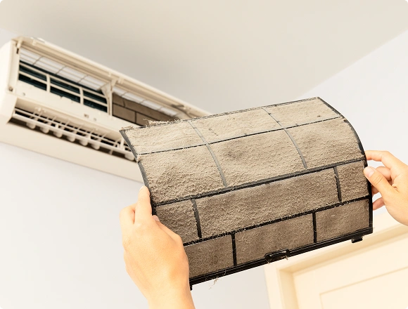 Dirty air conditioner filter covered in dust being removed from a wall-mounted AC unit