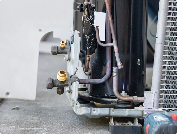 Close-up of compressor and copper pipes inside an outdoor air conditioner unit during repair