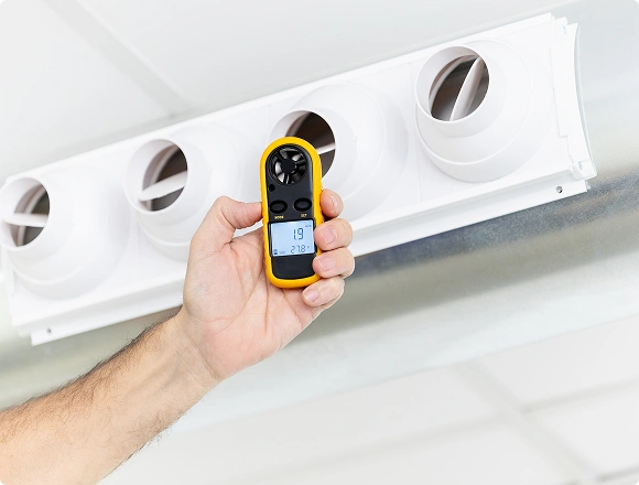 Technician measuring airflow from ceiling air vents using a handheld anemometer