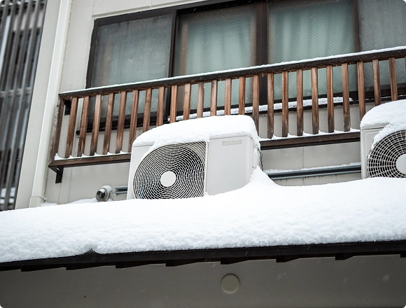 Outdoor air conditioner condenser unit covered with snow during winter on a residential building