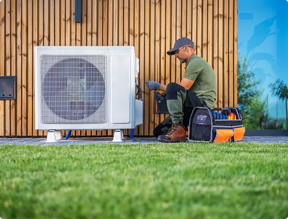 Technician servicing an outdoor air conditioning unit near a house.