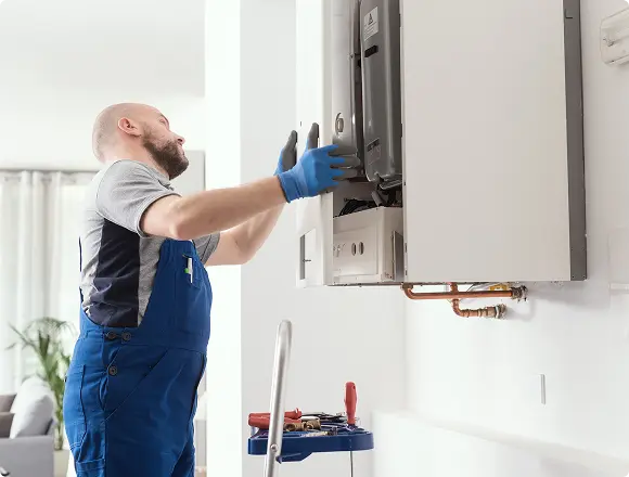Technician installing or servicing a wall-mounted boiler unit indoors.
