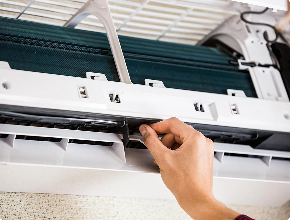 Close-up of a person cleaning the filter inside a wall-mounted air conditioner