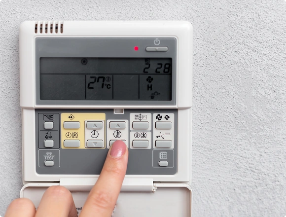 Close-up of a person adjusting the temperature on a wall-mounted air conditioner thermostat control panel