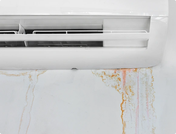 Wall-mounted air conditioner leaking water and leaving rust stains on the wall below