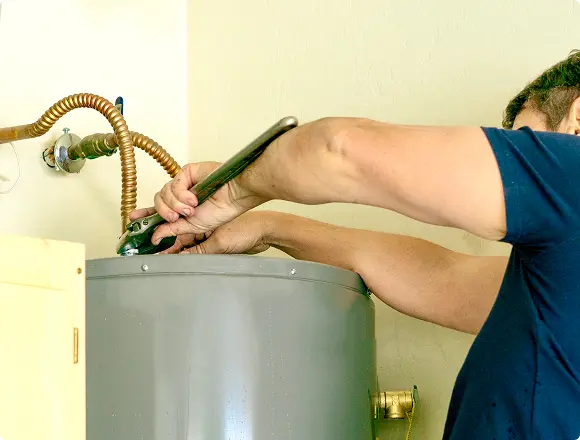 Technician repairing a water heater with tools.