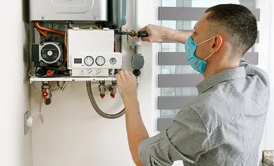 Technician wearing a mask servicing an open wall-mounted boiler unit.