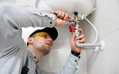 Technician tightening pipes under a water heater.