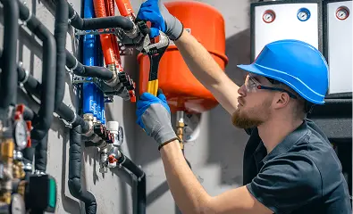 Technician adjusting valves and piping in an industrial heating system.