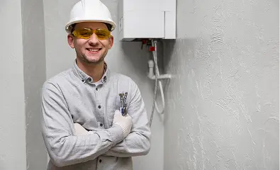 Technician standing with arms crossed near a wall-mounted water heater.