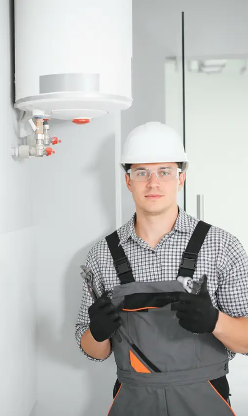 Technician standing next to a wall-mounted water heater and holding tools.