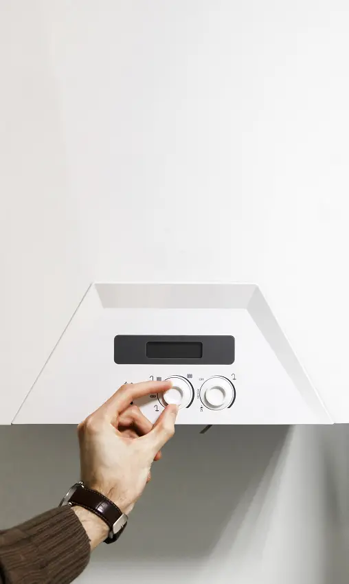 Hand adjusting temperature controls on a wall-mounted boiler.