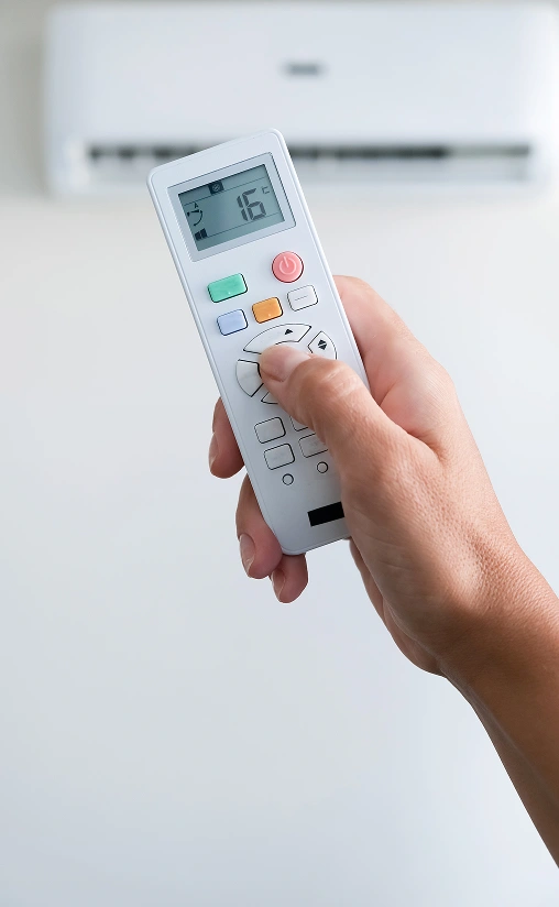 Hand holding a remote control to adjust the temperature of a wall-mounted air conditioner