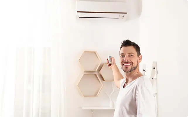 Man smiling while using a remote control to adjust a wall-mounted air conditioner.