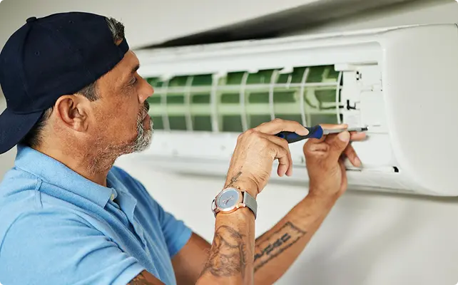 Technician using a screwdriver to service or repair a wall-mounted air conditioner.