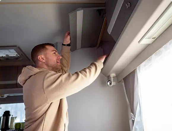 Man opening or adjusting an indoor unit or cabinet near the ceiling, likely performing maintenance on an air conditioning or ventilation system.