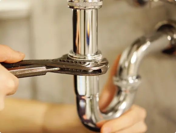 Close-up of a plumber tightening a pipe connection under a sink using an adjustable wrench.
