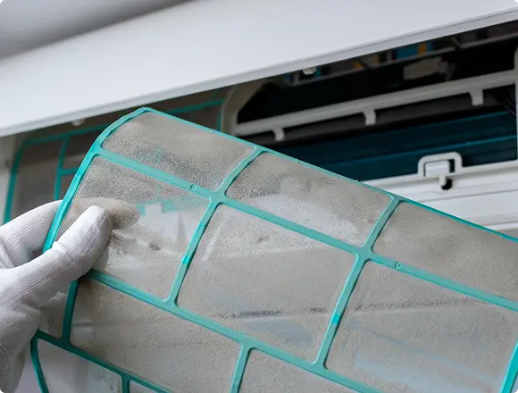 Hand holding a dirty air conditioner filter removed from the unit, indicating it needs cleaning or replacement.