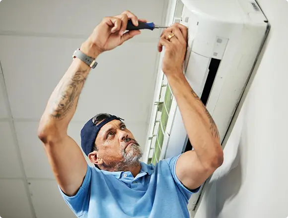 Technician repairing a wall-mounted air conditioner using a screwdriver.