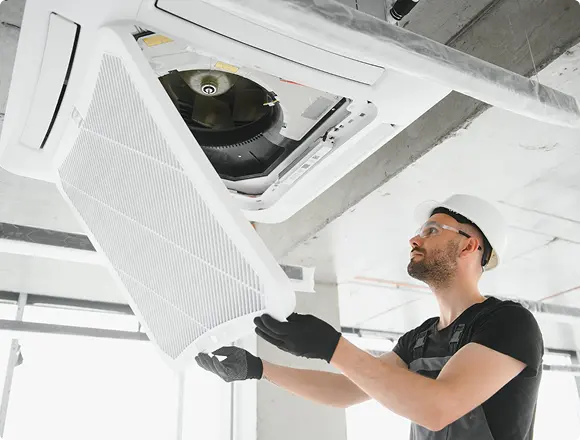 Technician opening and removing a ceiling-mounted air conditioning unit panel to access internal components for maintenance.