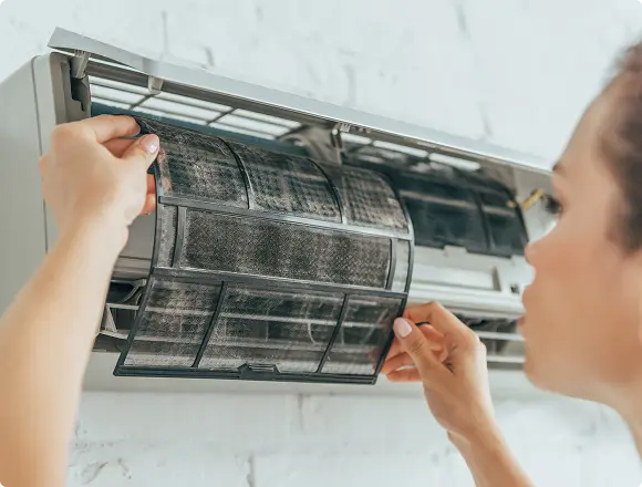 Person removing a dirty filter from a wall-mounted air conditioner for cleaning or replacement.