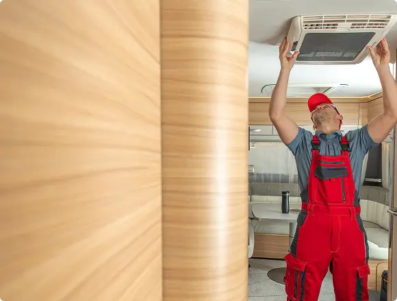 Technician in uniform installing or servicing a ceiling-mounted air conditioner inside a room.
