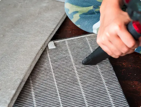 Person cleaning an air filter using a vacuum cleaner, removing dust and debris for maintenance.