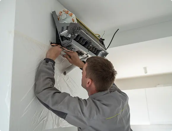Technician repairing internal components of a wall-mounted air conditioning unit.