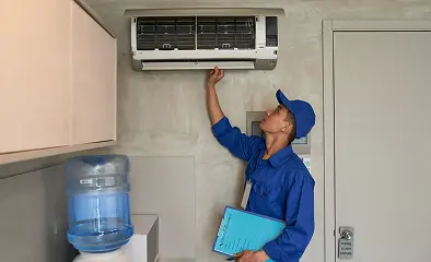 Technician inspecting a wall-mounted air conditioner while holding a clipboard.