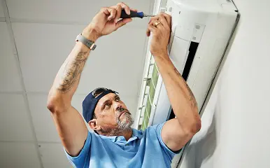Technician repairing a wall-mounted air conditioner using a screwdriver.