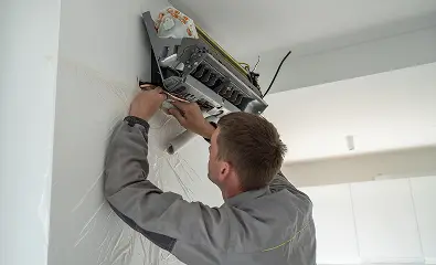 Technician installing or repairing a wall-mounted air conditioning unit.