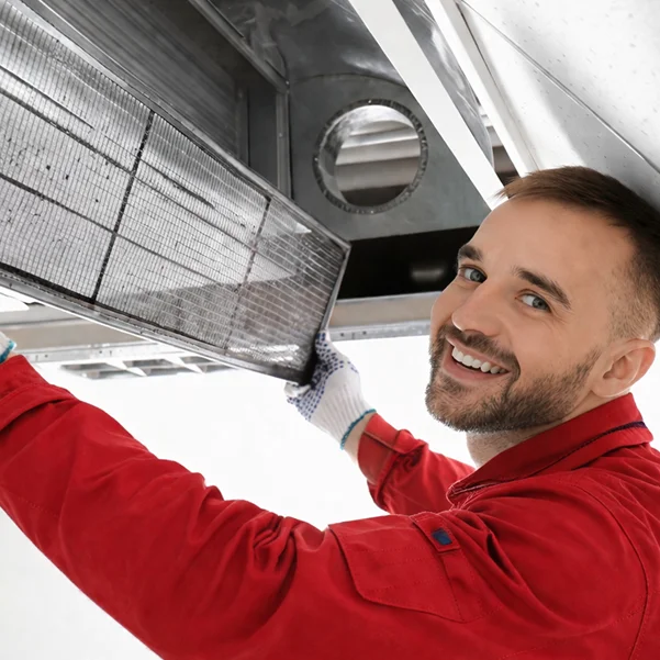 Smiling worker in red uniform replacing ceiling air duct filter