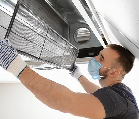 Technician with mask and gloves cleaning air duct filter