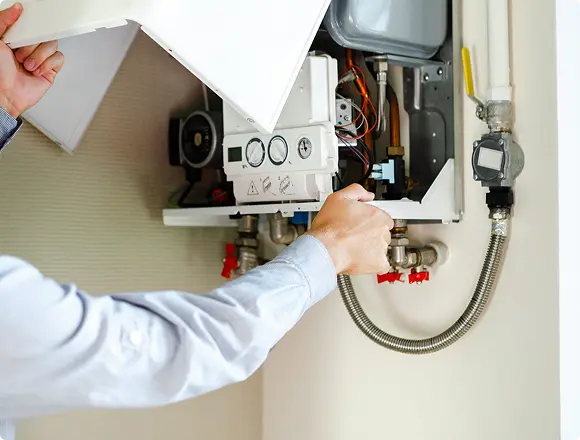 A technician opening the panel of a wall-mounted gas boiler to inspect its internal components and pipe connections