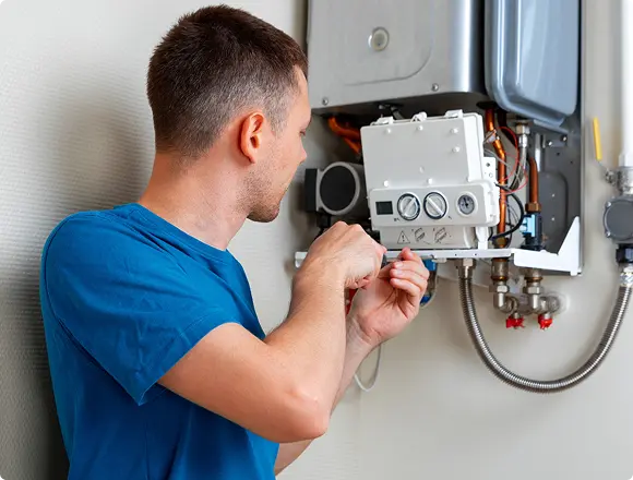 A technician in a blue shirt adjusting the control panel of a wall-mounted gas boiler