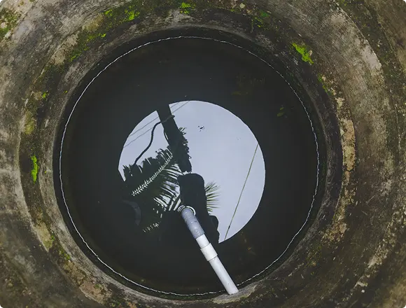 Aerial view looking down into a concrete water well with a pump pipe and sky reflection on the water surface